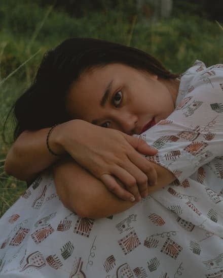 Person resting on folded arms outdoors, wearing a white patterned shirt, with a calm expression.