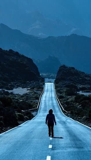 Person walking alone on a wet mountain road at dusk, with misty blue hills in the background.
