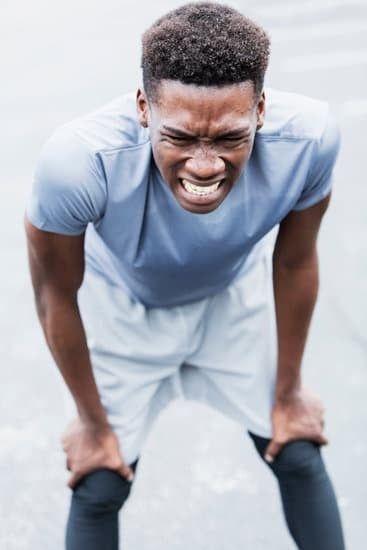 Man bent over with hands on knees, grimacing in workout clothes on a light background