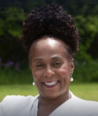 Smiling person in white shirt outdoors with greenery and flowers in the background