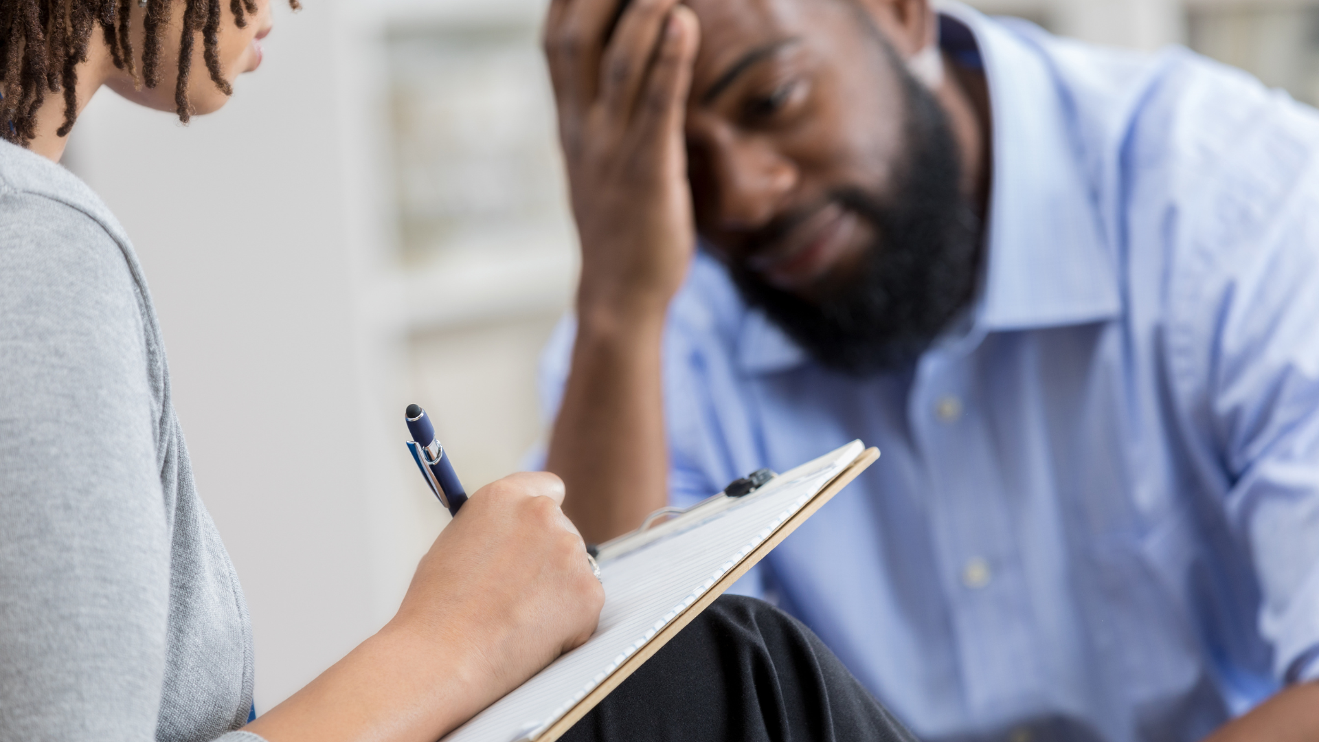 Counselor taking notes while speaking with a distressed client in a therapy session