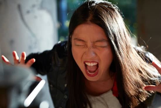 Person shouting with eyes closed, leaning forward in a dark jacket indoors