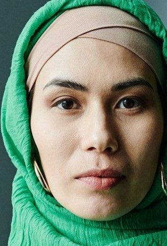 Close-up portrait of a person in a green hijab and beige headband, looking straight ahead with a neutral expression.