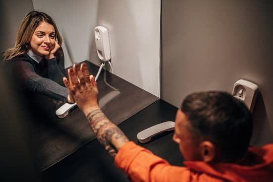 Man in orange shirt reaching toward a smiling woman on a monitor in a video call interface