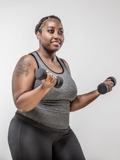 Woman in gray tank top and black leggings holding dumbbells against a plain background