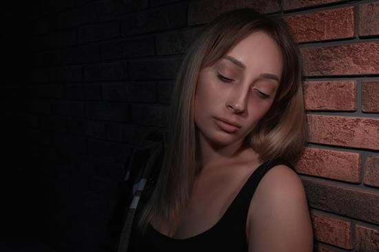 Woman with closed eyes leaning against a brick wall in dim light