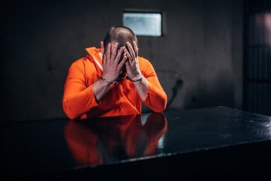 Person in an orange hoodie sits at a table with their face in their hands, looking distressed.