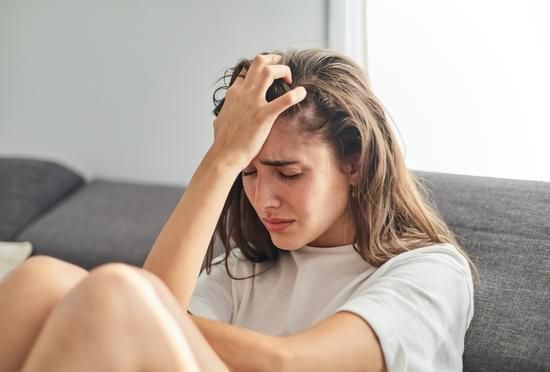 Woman sitting on a couch, holding her head with a pained expression.