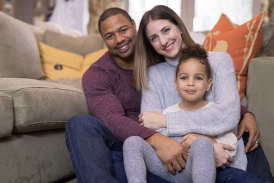 Family of three sitting on a couch, smiling and hugging in a cozy living room.