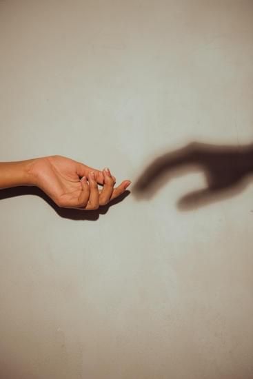 Two hands reaching toward each other, one real and one shadow, on a beige background