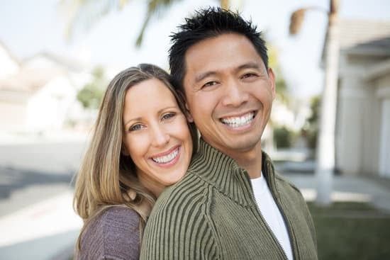 Smiling couple posing outdoors in front of a house, with the woman leaning against the man.