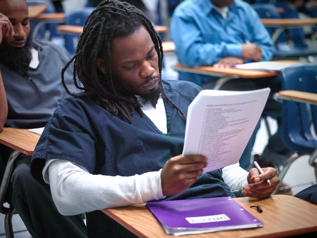 Student reading a paper in a classroom, with a purple folder on the desk.