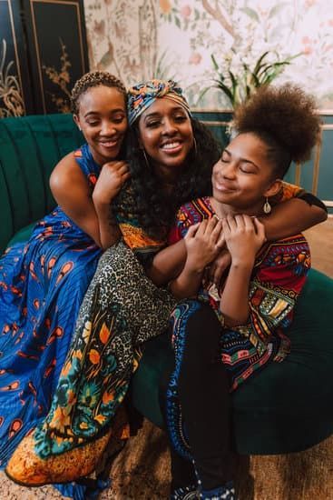 Three friends smiling and hugging on a teal couch in a colorful living room
