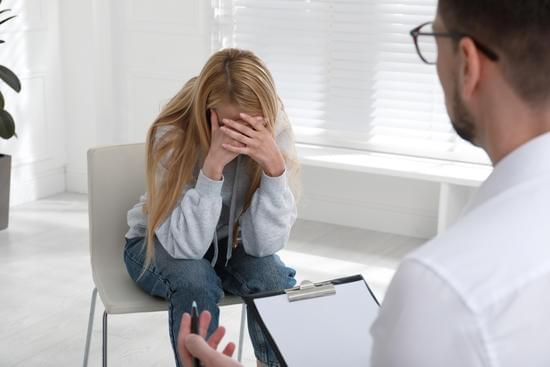 Counselor talks with upset client covering her face in a bright office