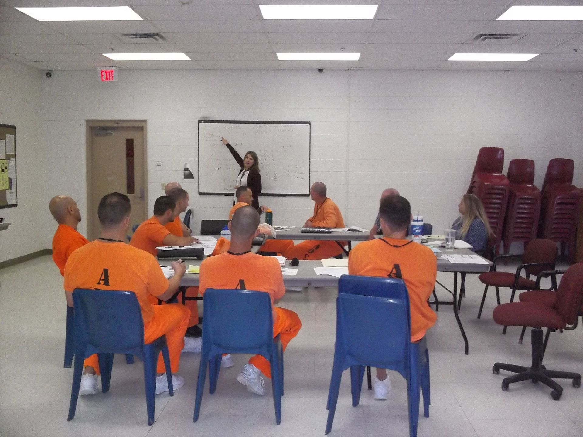 People in orange uniforms seated in a classroom, facing a whiteboard and instructor.