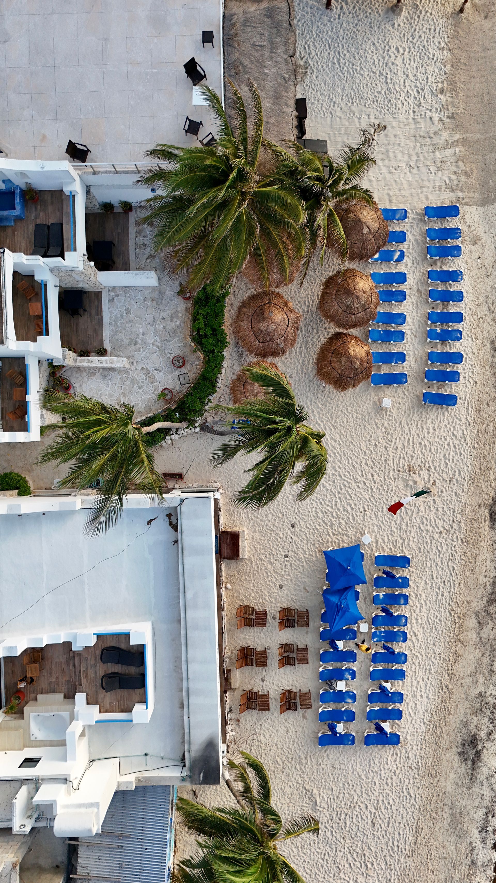 Una vista aérea de una playa con sillas azules y sombrillas.
