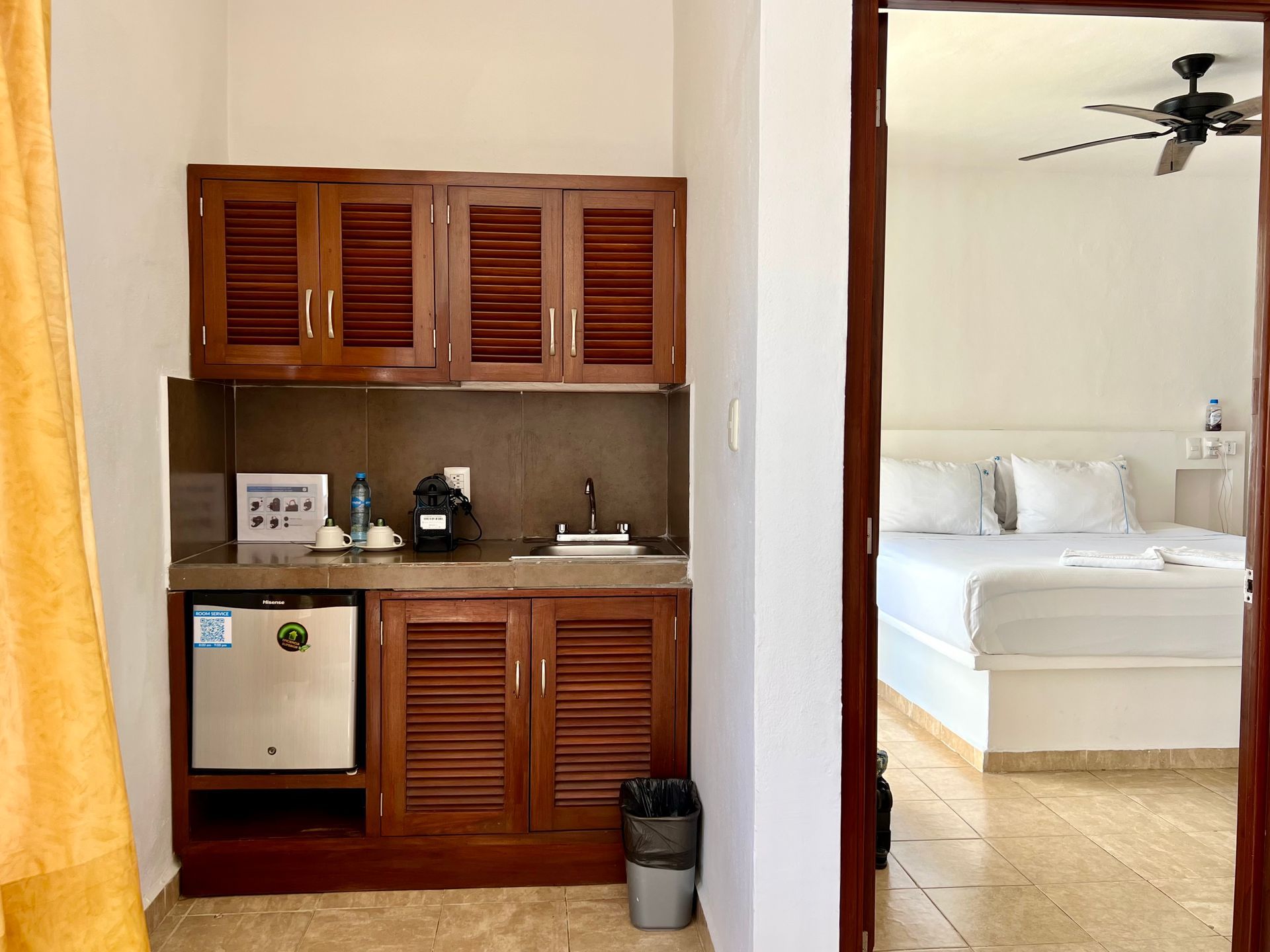 Una cocina con fregadero, refrigerador y armarios en una habitación de hotel al lado de una cama.