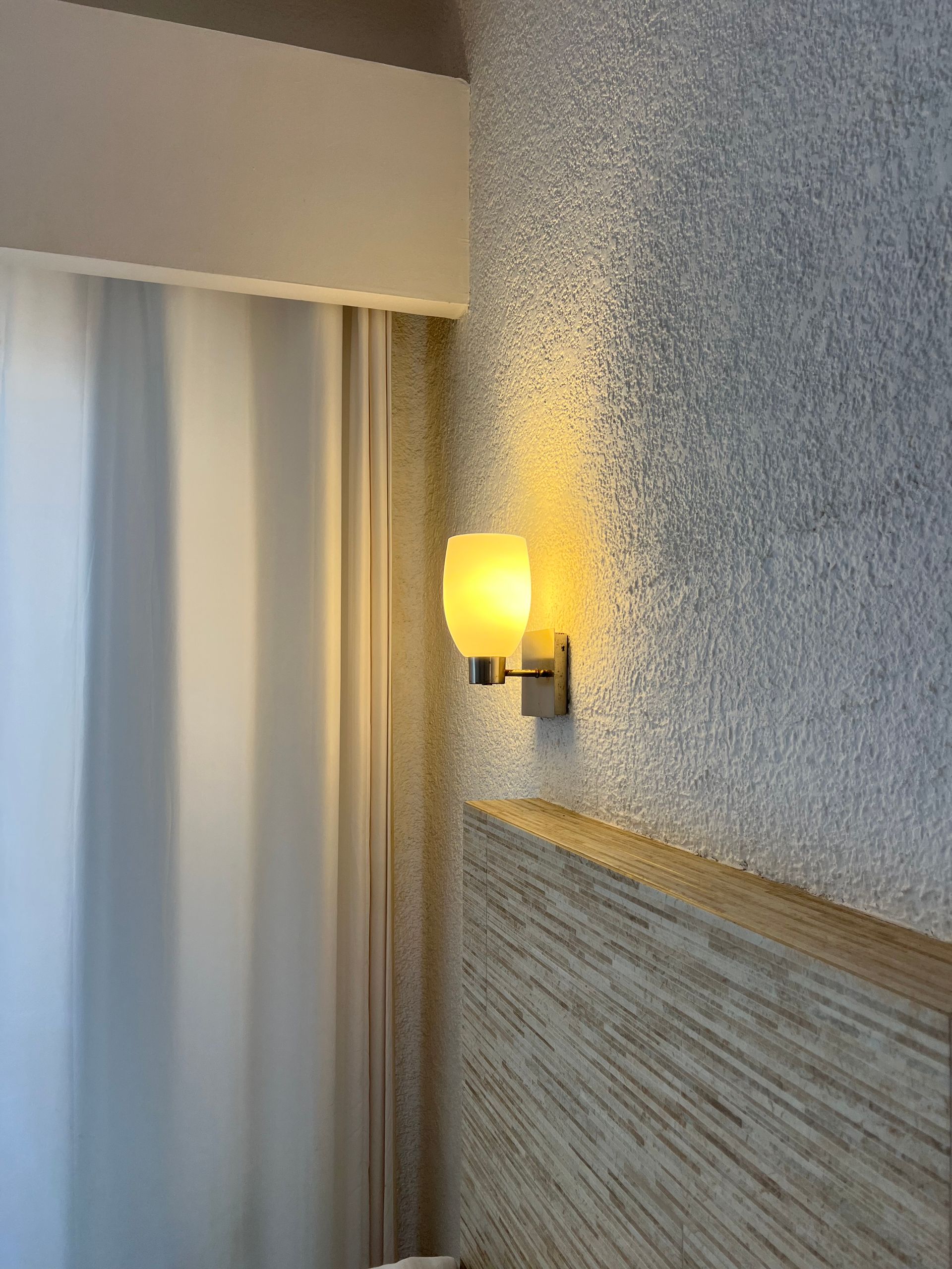 Hay una luz en la pared al lado de una ventana.