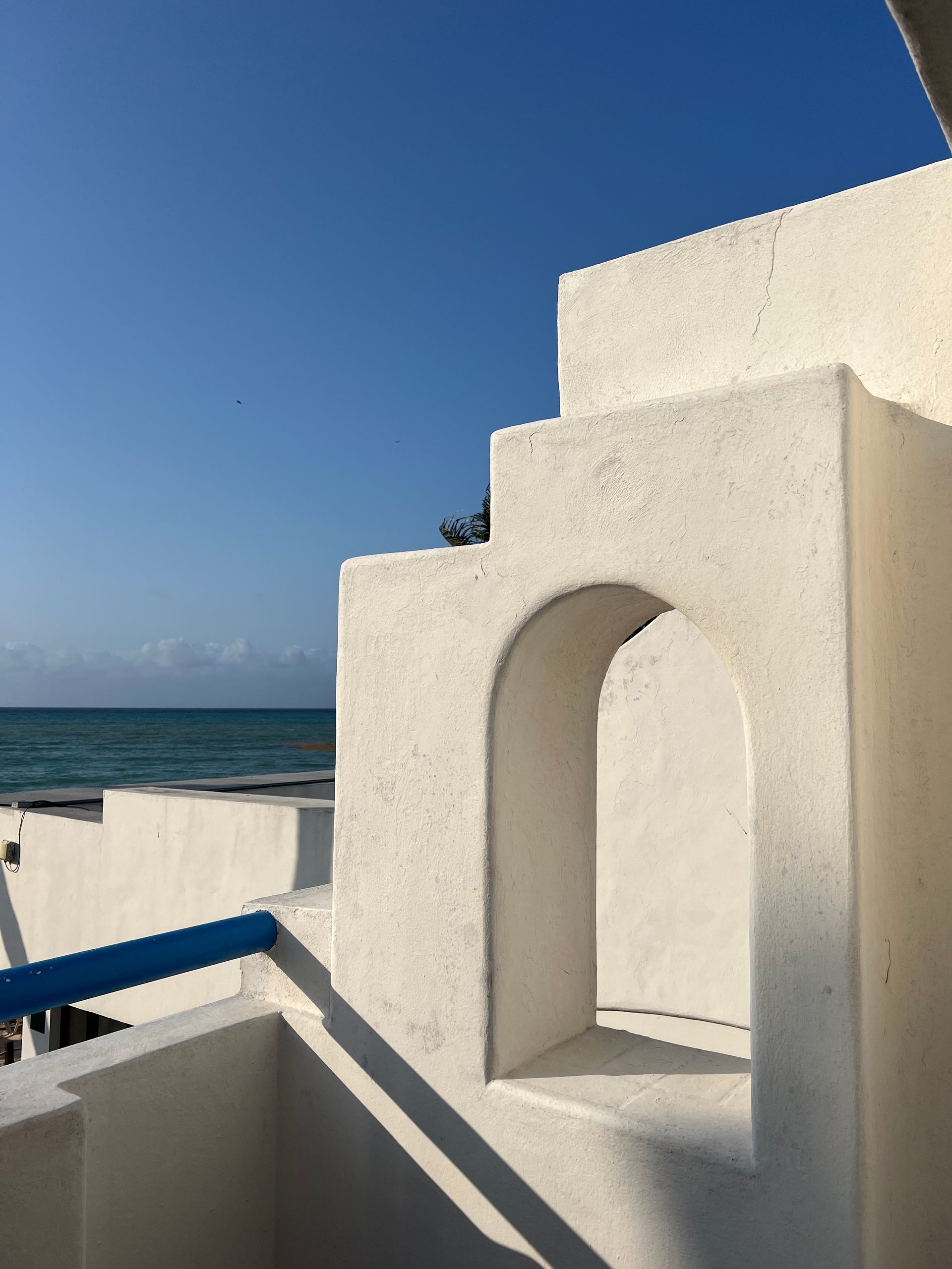 Un edificio blanco con una barandilla azul con vistas al océano.