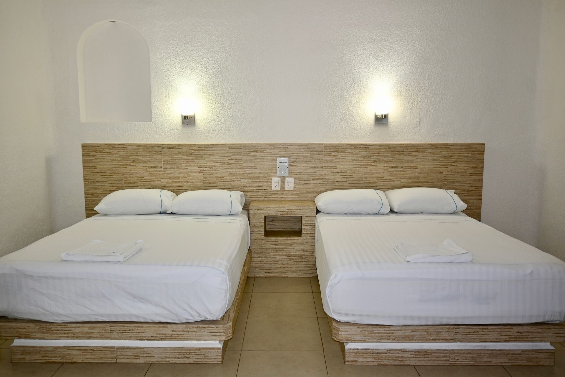 Una habitación de hotel con dos camas y cabecero de madera.
