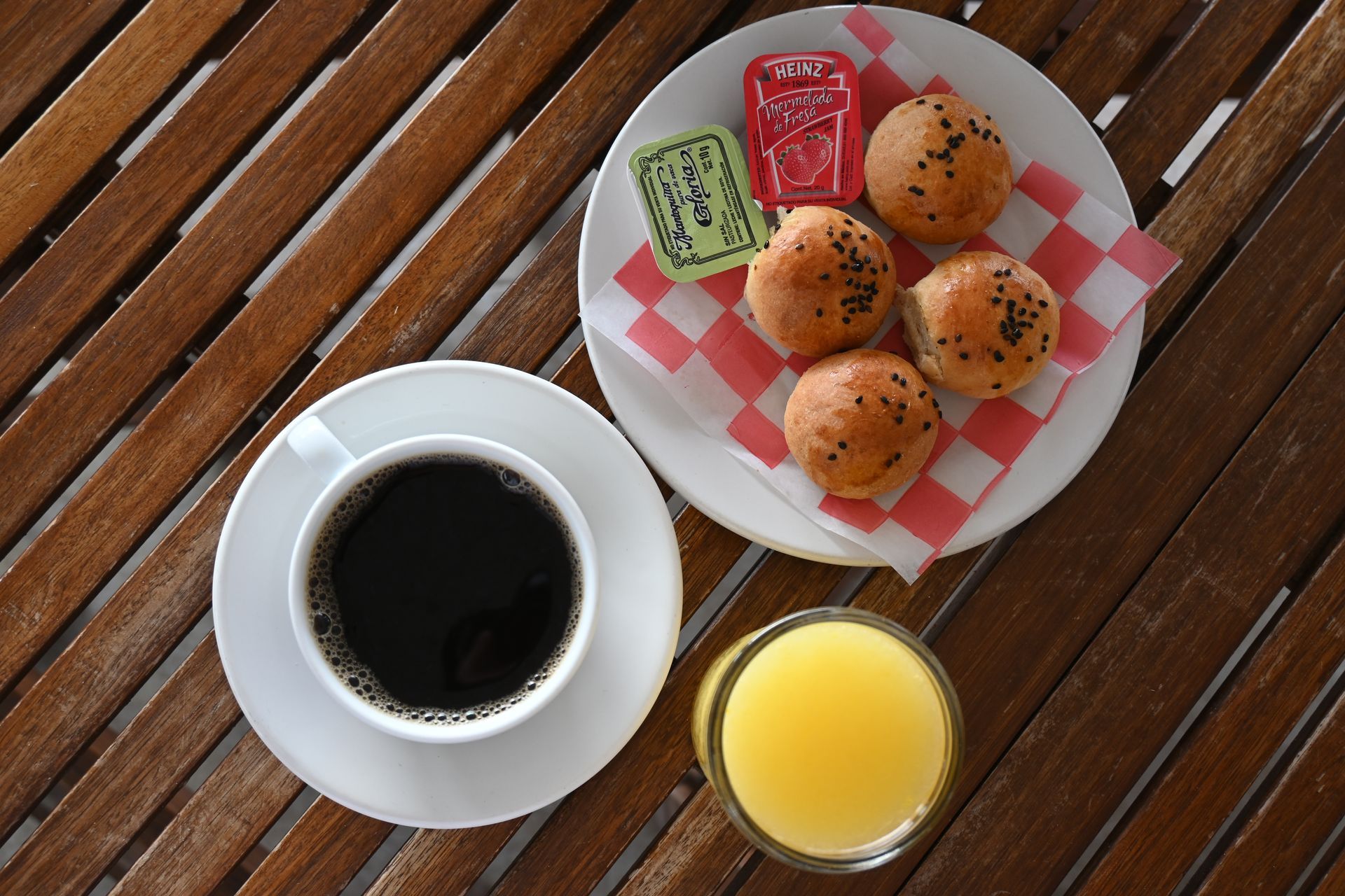 Una taza de café junto a un plato de comida y un vaso de jugo de naranja.