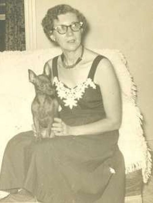 Woman in dress sits with small dog on her lap.
