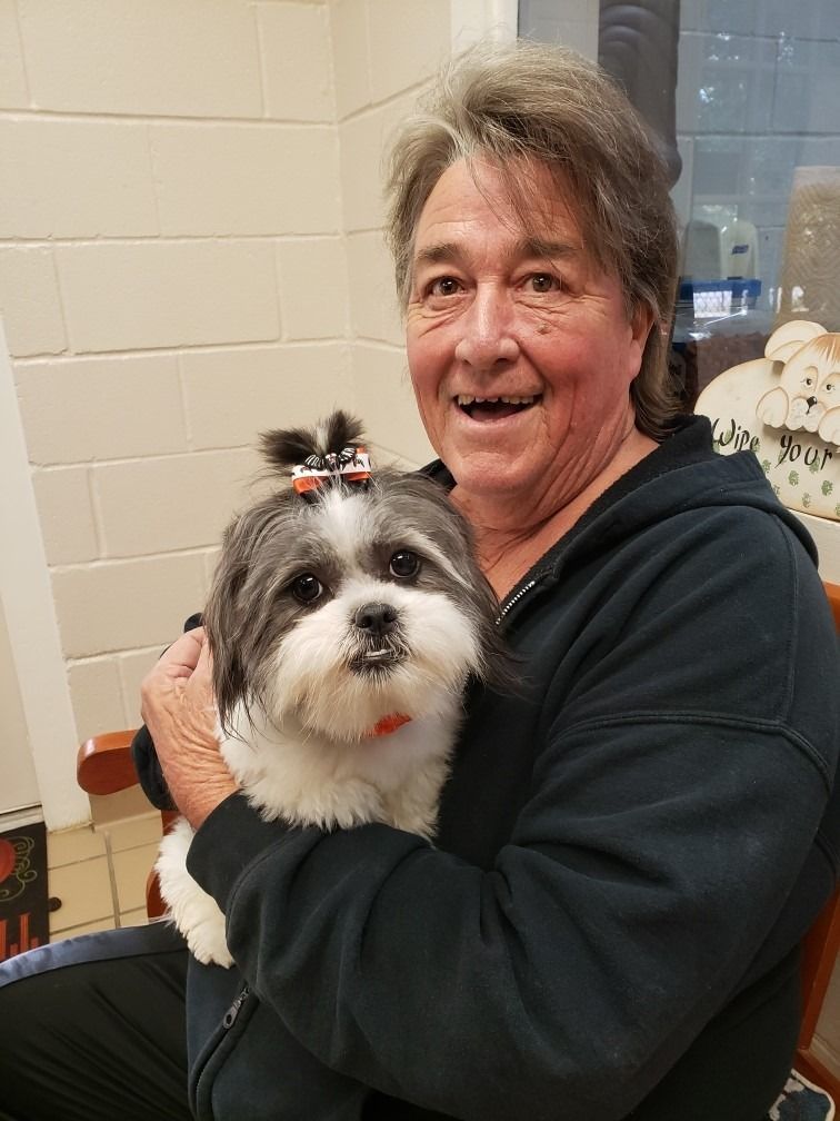 Person smiles while holding a small black and white dog with a bow in its hair.