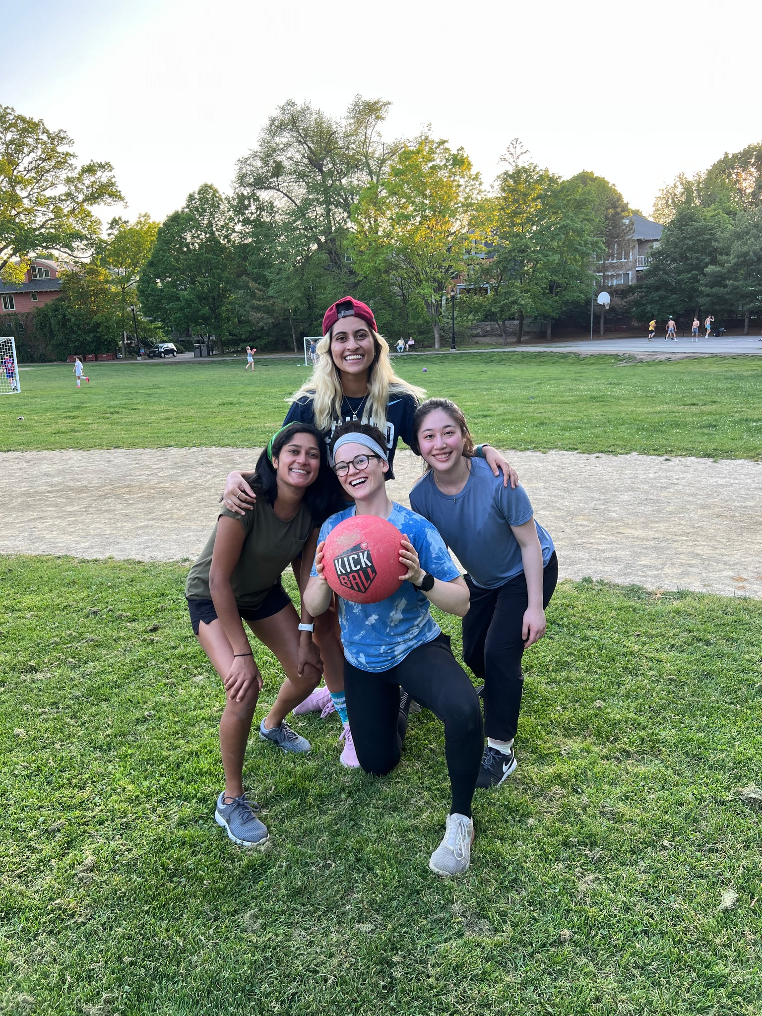 Four people pose with a red ball on a grassy field; one kneels, the others stand, smiling.