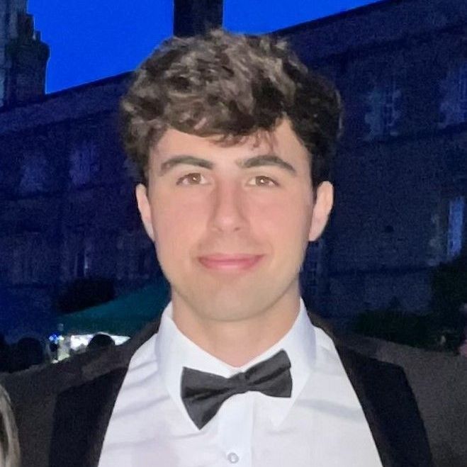 Man in tuxedo smiling, wearing a black bow tie, outside at night.