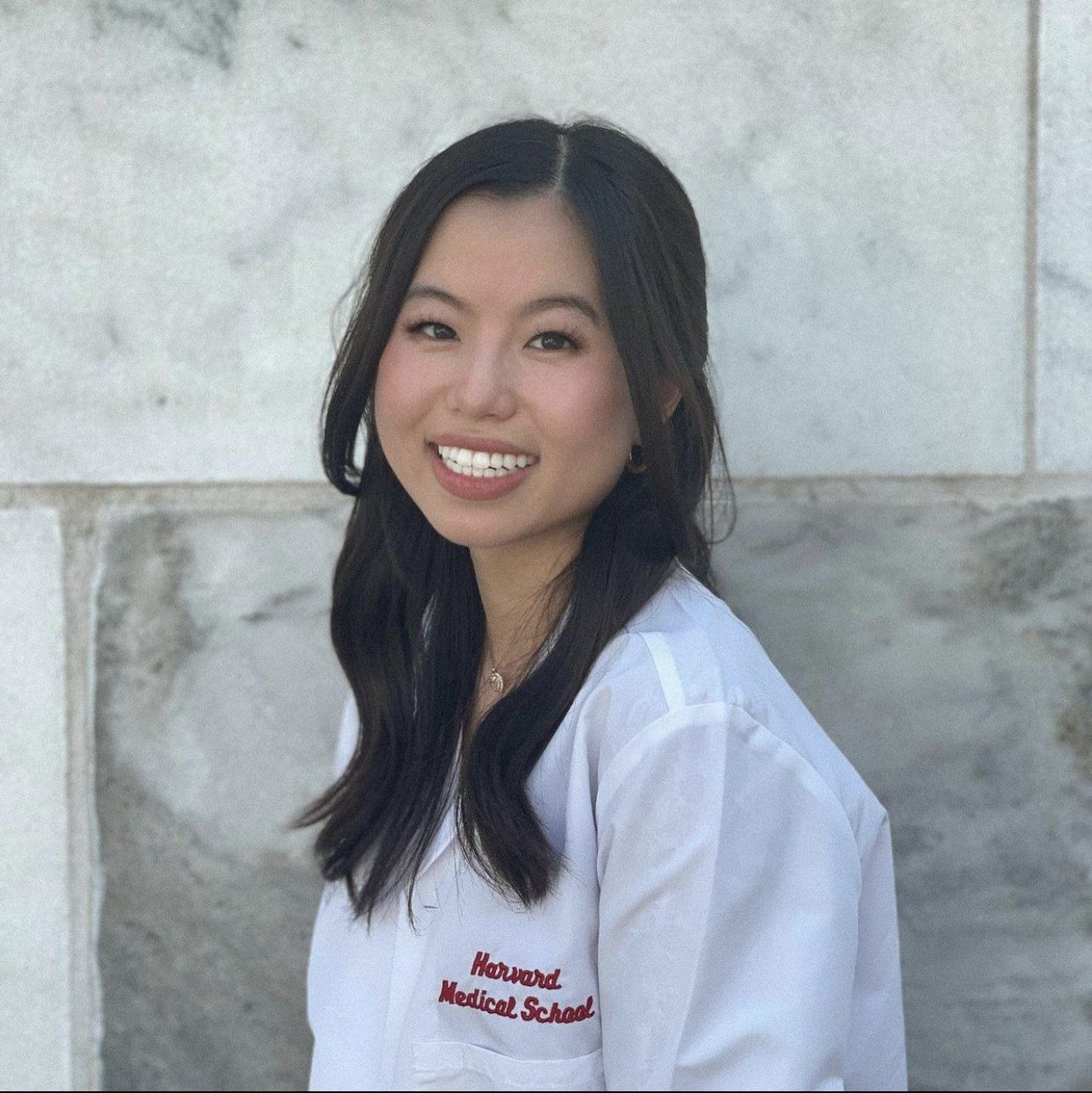 Woman in a white coat smiling, standing in front of a marble wall. 