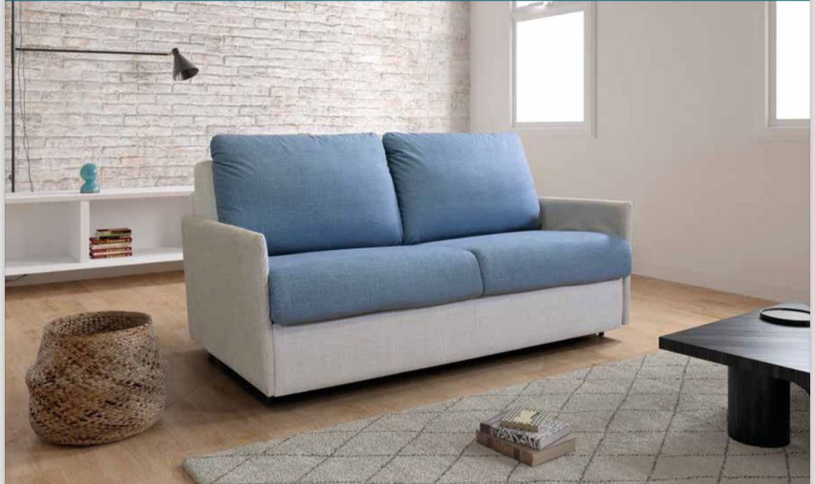 In una stanza luminosa con una parete di mattoni bianchi, un divano a due posti con cuscini blu e base grigio chiaro è collocato.