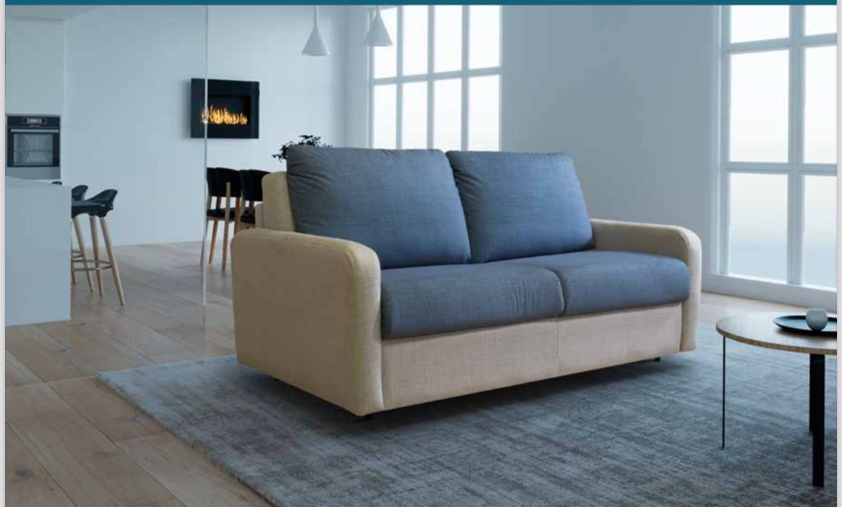 Un divano bicolore con cuscini blu e struttura beige chiaro, posizionato su un tappeto grigio in un luminoso soggiorno moderno.