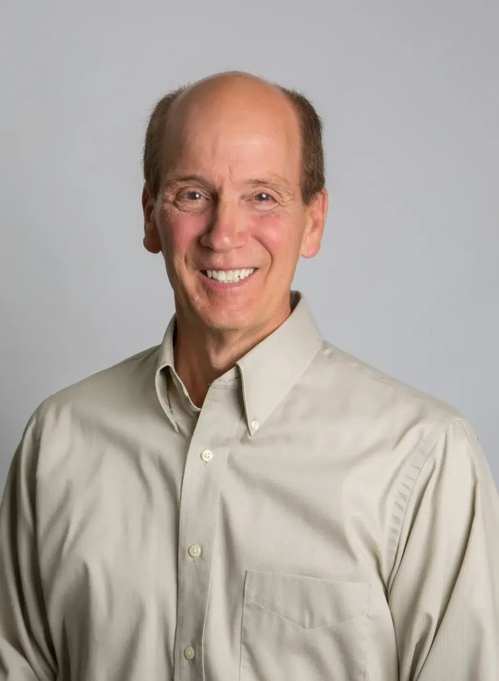 Smiling man with fair skin, light brown button-down shirt, neutral background.