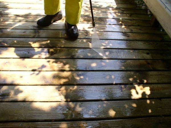 Person in yellow rain gear power washing a wooden deck, creating a wet area in Madison, Wisconsin.