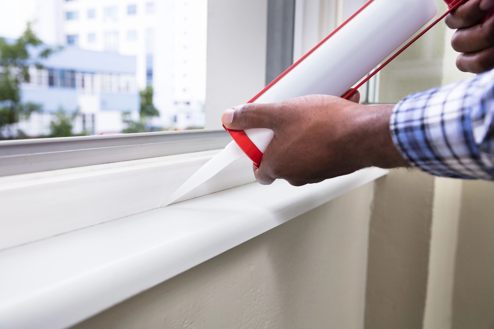 Person using a caulk gun to seal the edge of a window in Madison, Wisconsin.