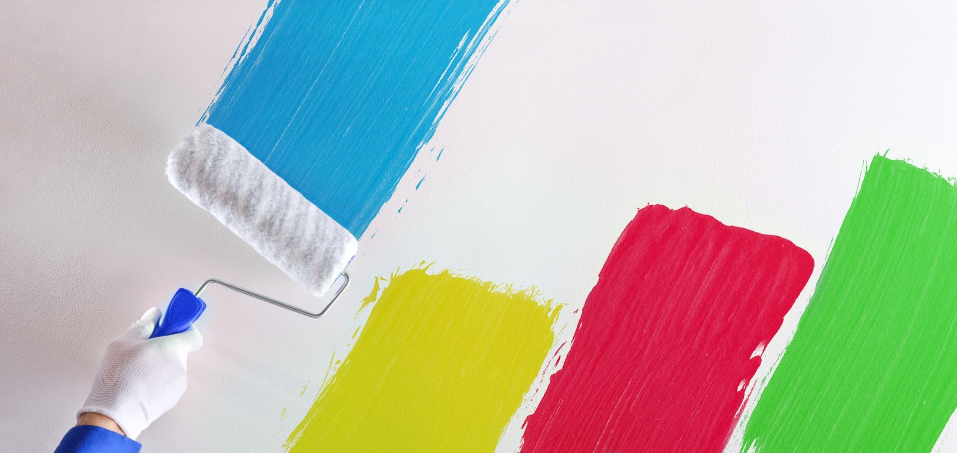 Hand painting a white wall with blue, yellow, red, and green paint, using a paint roller.