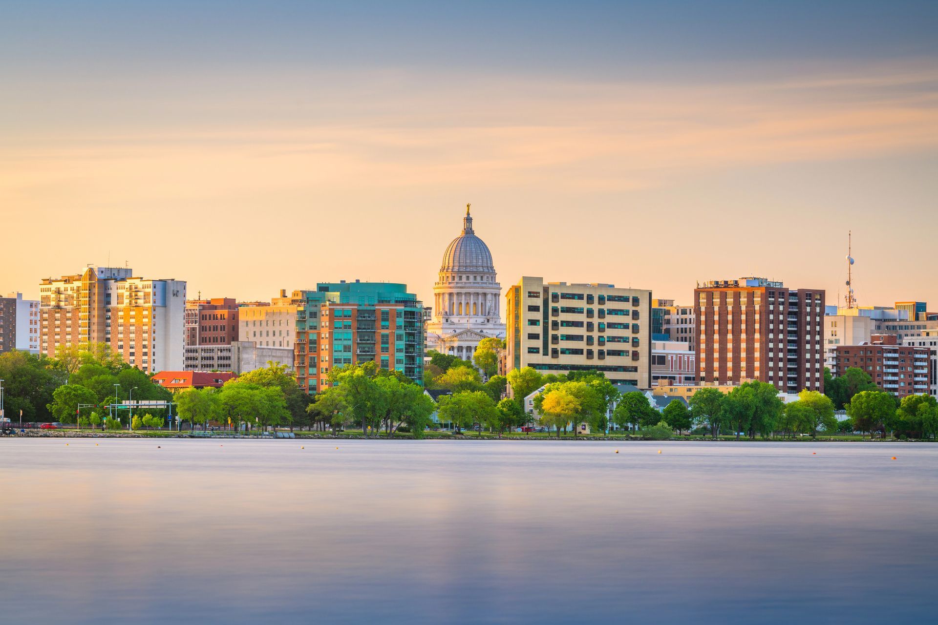 City skyline with a domed building in the center, reflecting in a lake under an orange sky in Madison, Wisconsin.