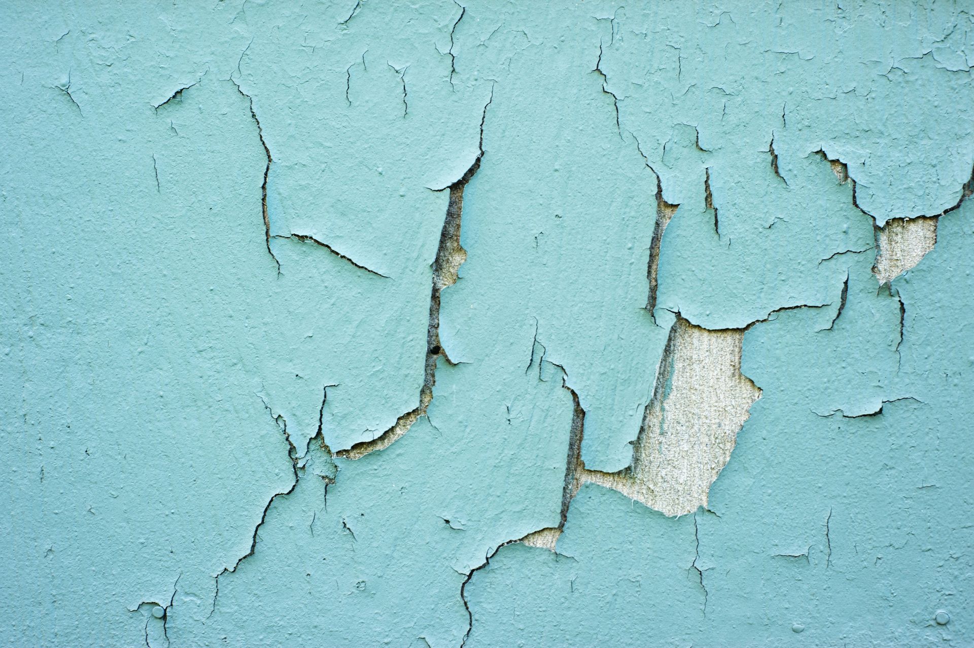 Cracked turquoise paint on a textured wall, revealing the underlying concrete in Madison, Wisconsin.