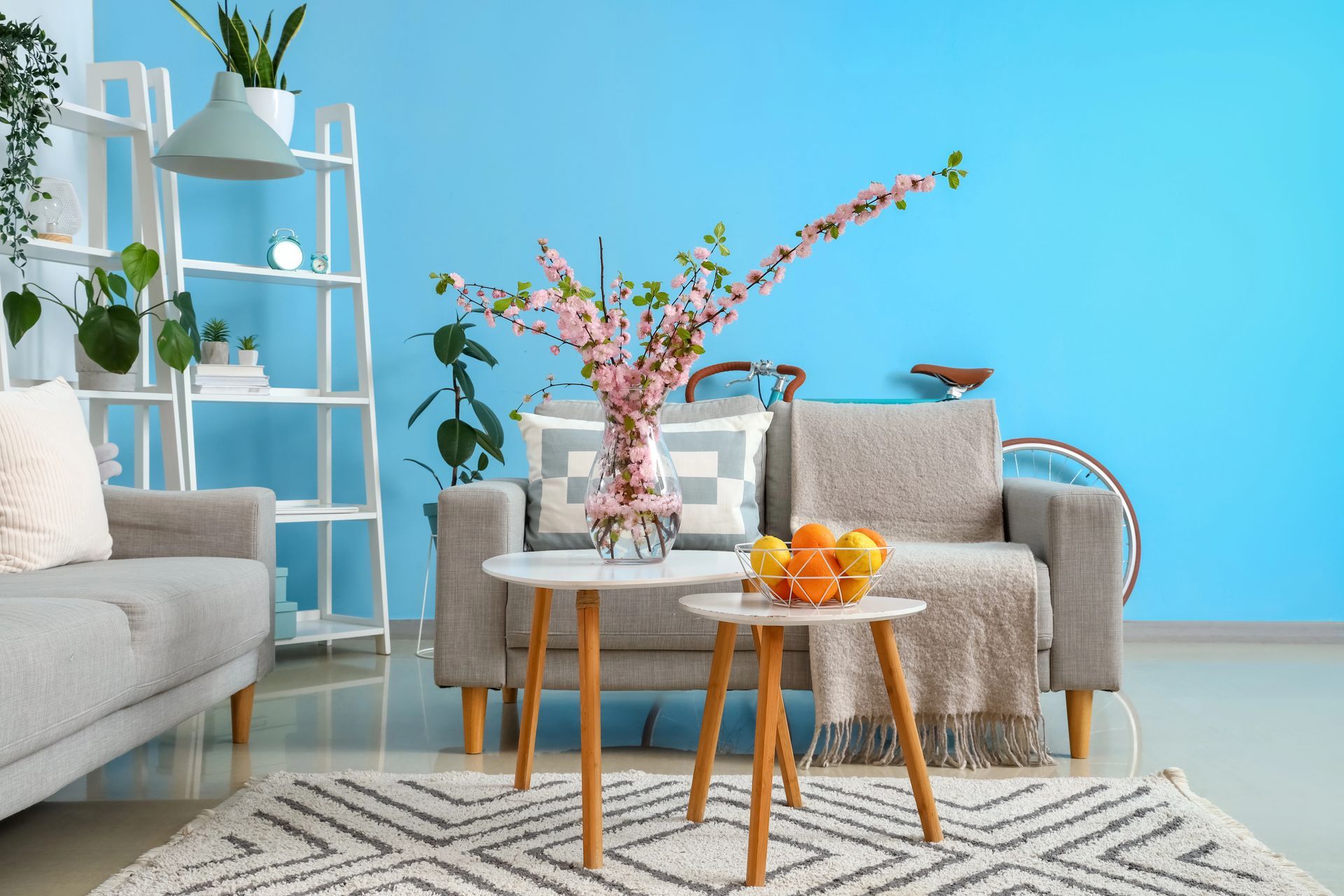 Living room with blue wall, gray sofas, wooden tables, rug, flowers, and bicycle in Monona, Wisconsin.