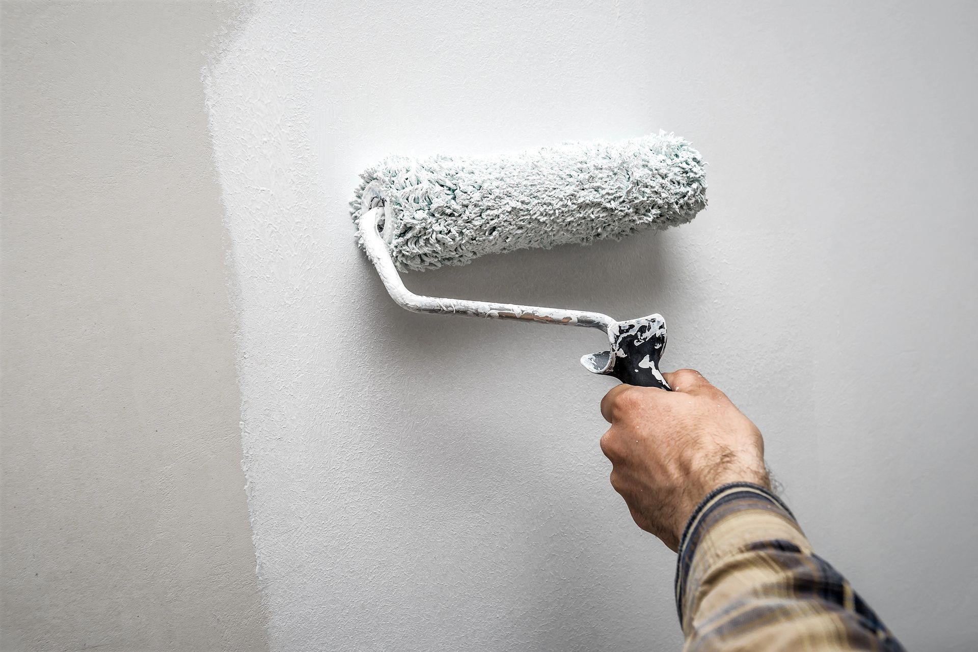 Person using a paint roller to apply white paint to a wall in Madison, Wisconsin.