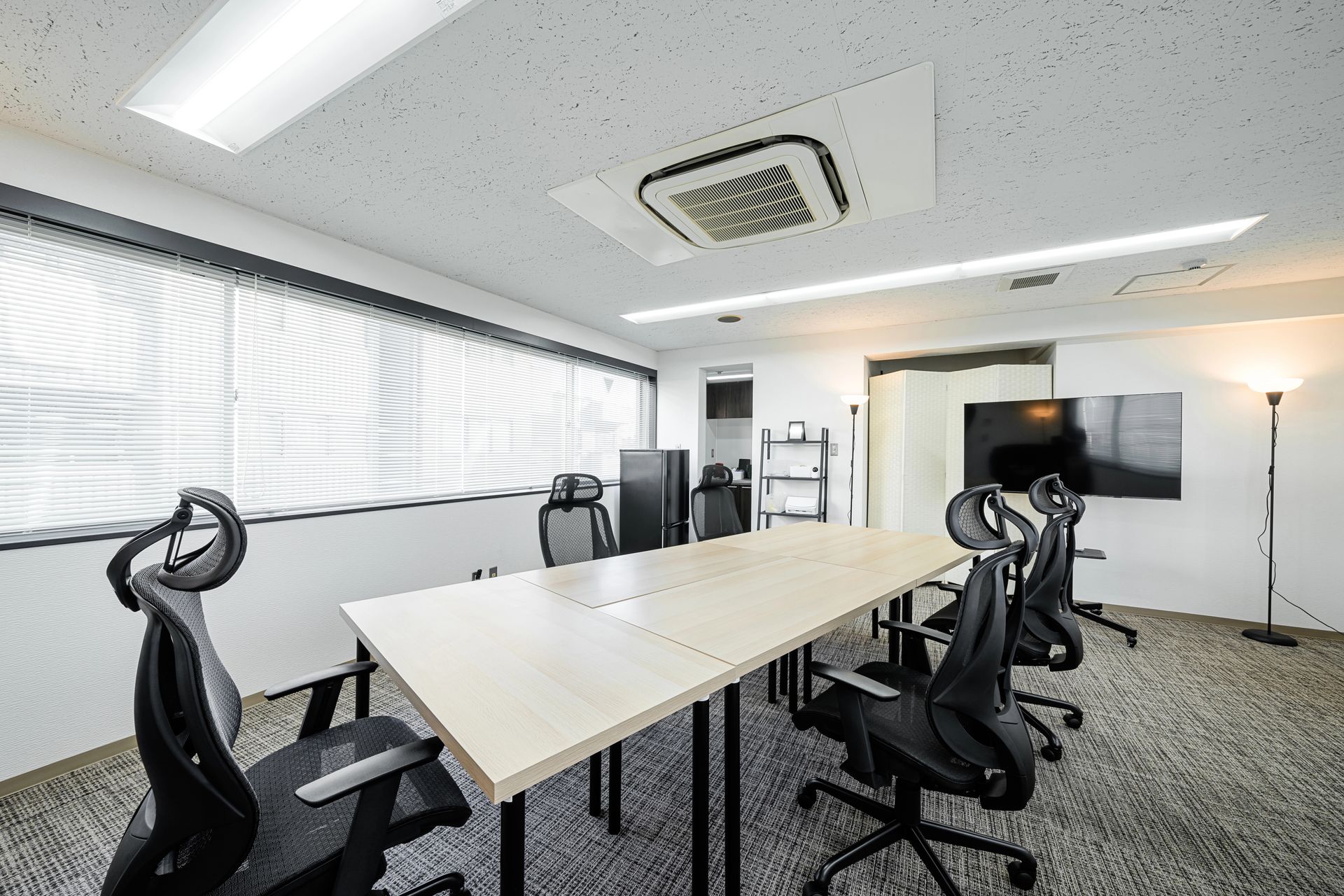 Conference room with long table, office chairs, and large screen. Window with blinds and ceiling air vent visible in Madison, Wisconsin.