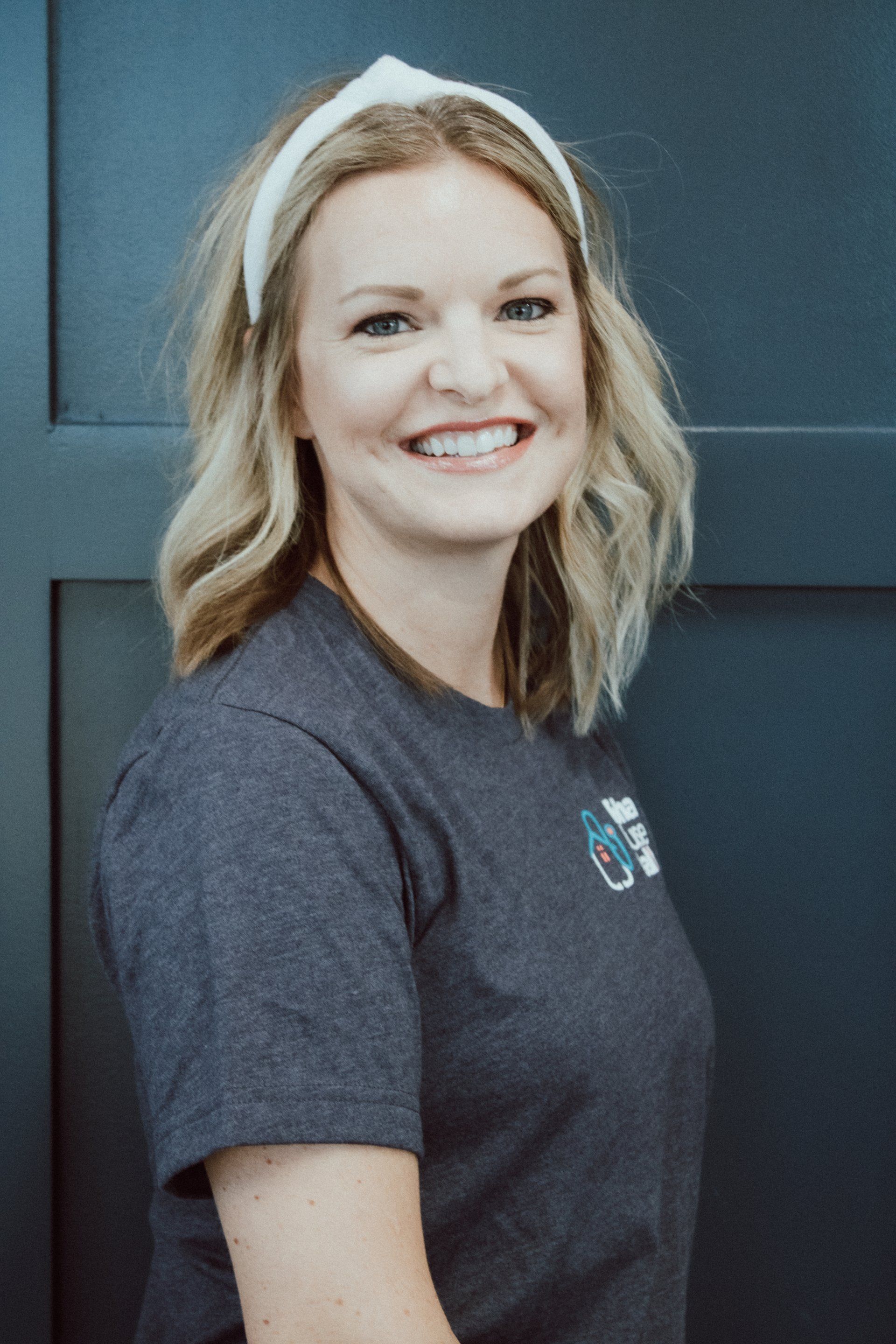 A woman wearing a headband and a gray shirt is smiling.