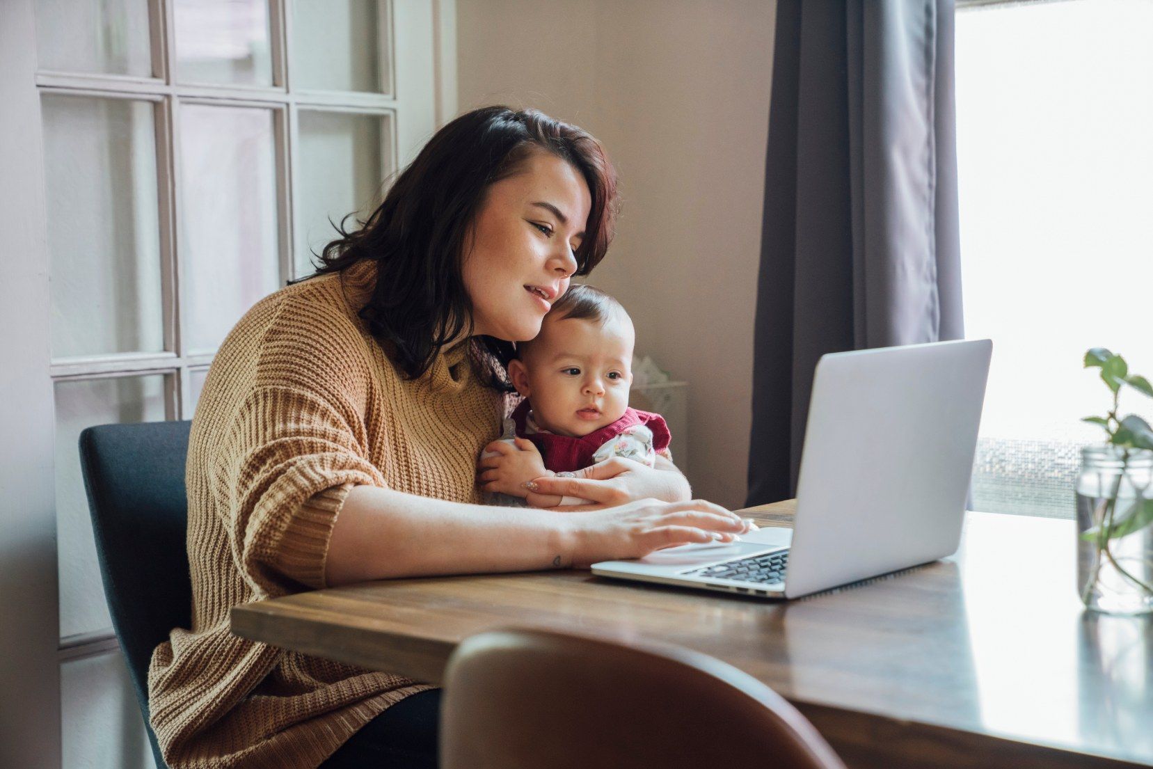 A woman is holding a baby while using a laptop computer.