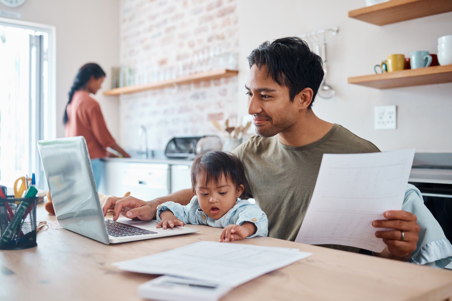 A man is sitting at a table with a baby and a laptop.