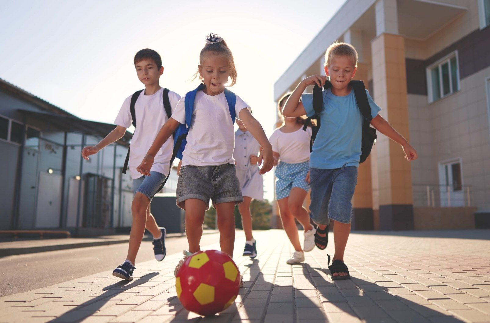 A group of children are playing with a soccer ball on the sidewalk.
