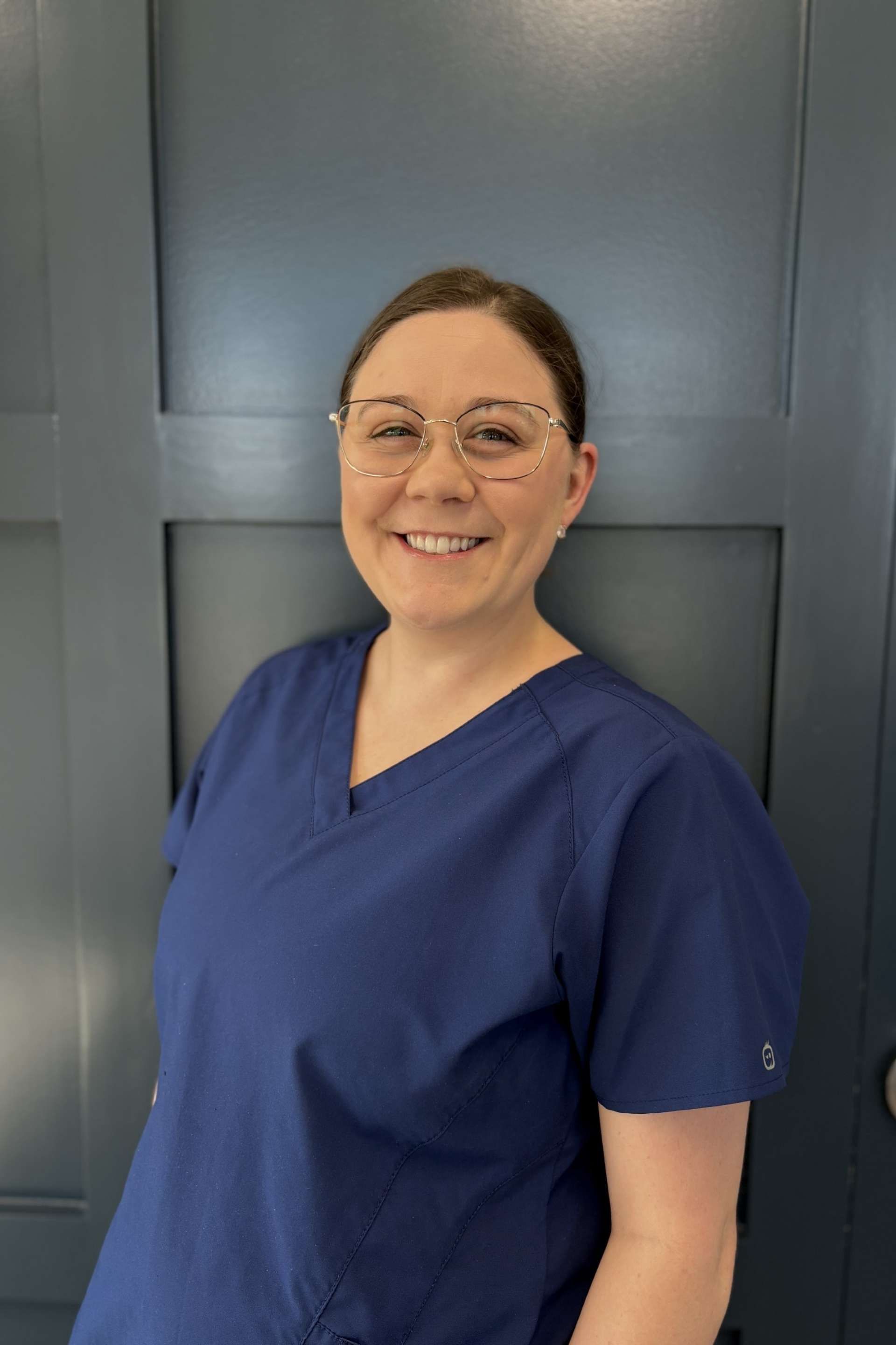 Person in blue scrubs smiling in front of a dark door