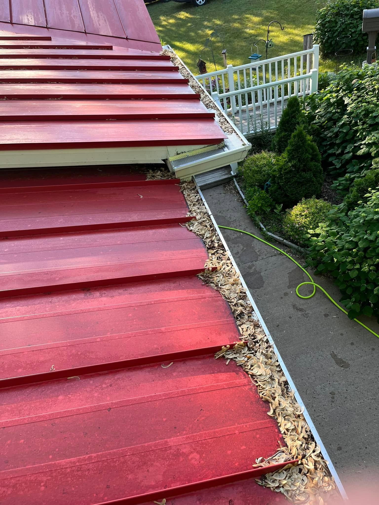 Red metal roof with snow guard and white railing beside a green hillside walkway
