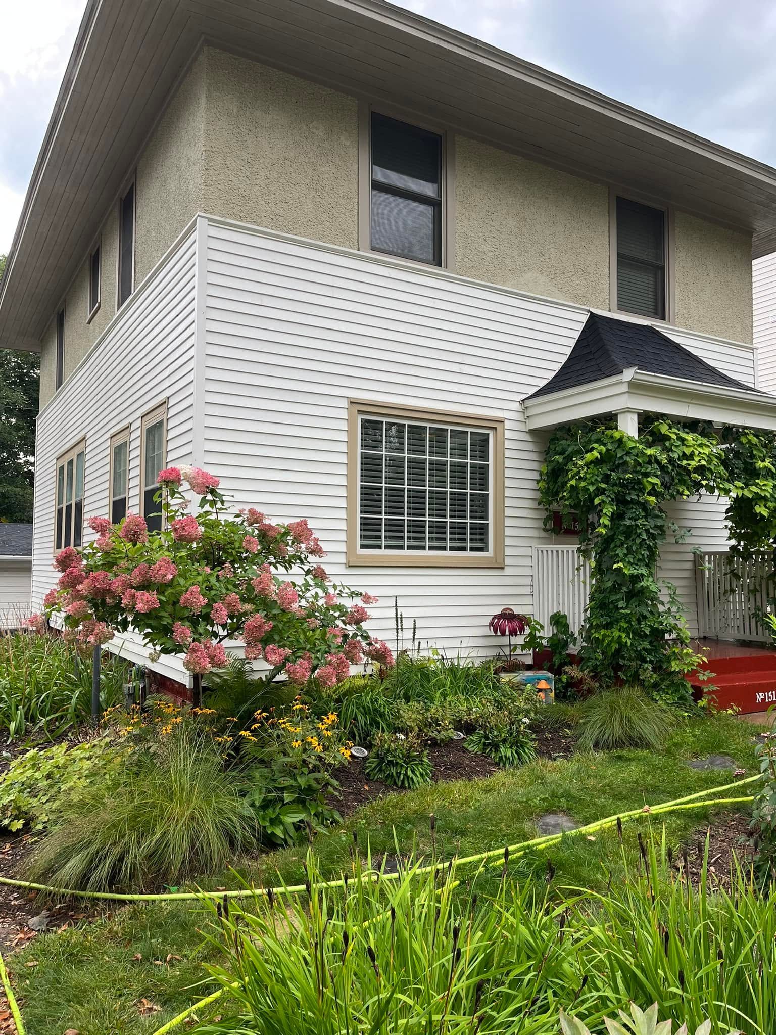 Two-story house with white siding, striped awning, and lush garden flowers in the foreground