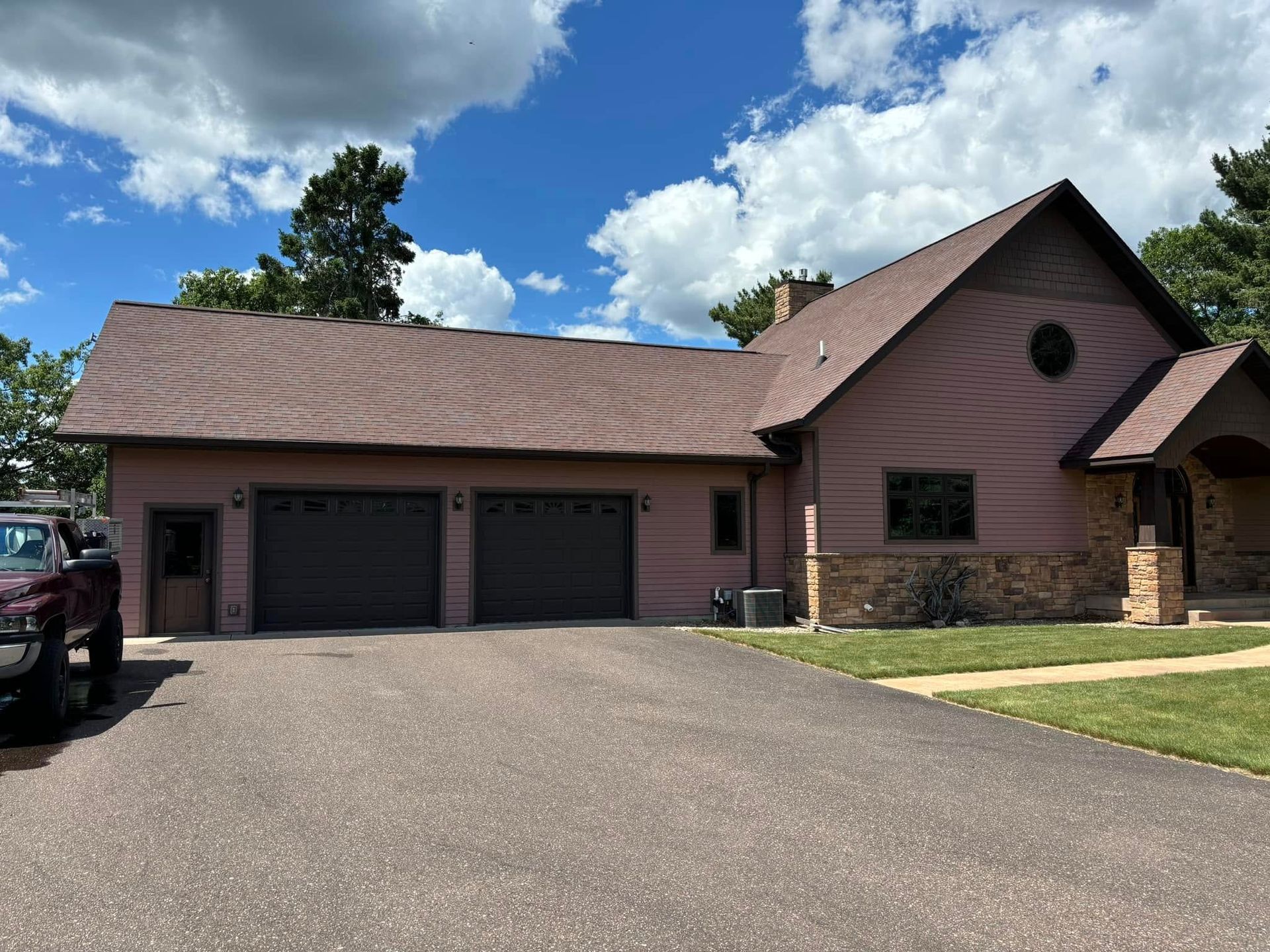 Suburban house with three-car garage, brown roof, and a wide driveway under a blue sky.