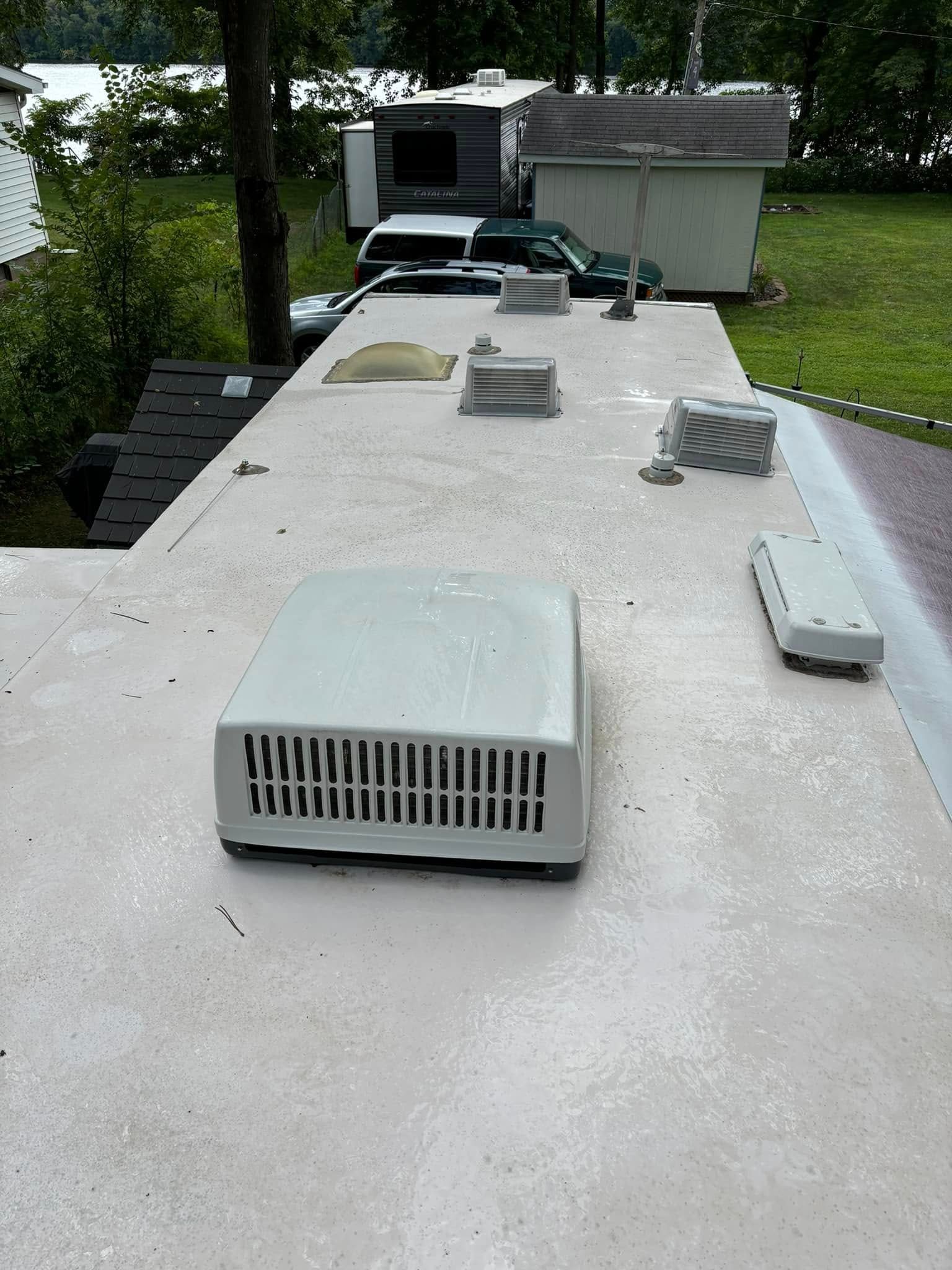 Flat white rooftop with several HVAC vents and units, viewed from the end toward trees and a parked vehicle.